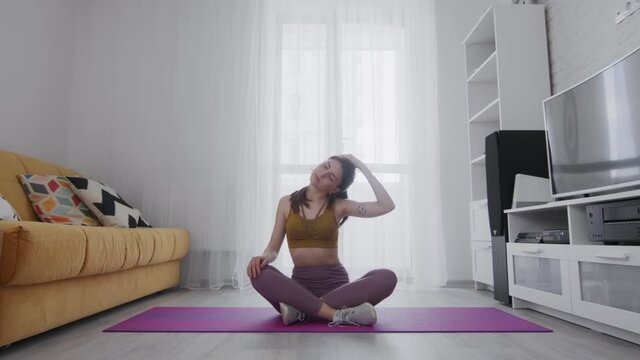 Young beautiful woman with tattoo stratching neck on mat at home