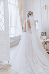 the bride in a beautiful dress stands at the window in a bright room
