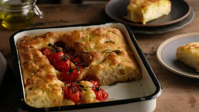 Female hands cut focaccia, prepare Italian bread - focaccia with olive oil, tomatoes, seasonings, rosemary and sea salt. Dough for bread. Preparing focaccia - Pizza. Close-up.
