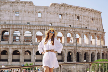 Obraz premium Piękna młoda kobieta w kolorowy moda sukienka sama przed Koloseum w Rzymie o zachodzie słońca. Atrakcyjna dziewczyna turystycznych zdejmując elegancki słomkowy kapelusz.