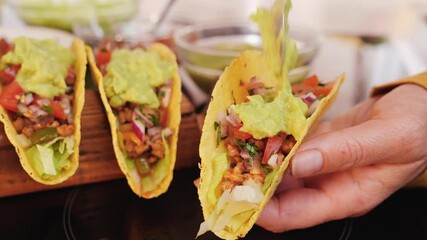 Woman hand stuffing hard taco shells - adding the guacamole topping, holding the shell, camera orbit, close up. Phases of making tacos.