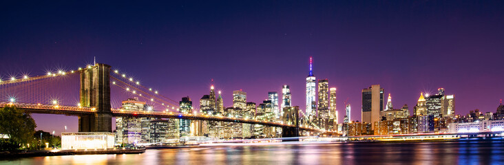 Stunning panoramic view of the Brooklyn Bridge and the illuminated Manhattan's skyline at dusk during the Covid-19 lockdown. New York City, United States.