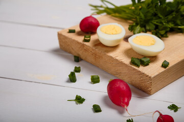 Radish, green onions, parsley, eggs on kitchen chopping board on white wooden background. Copy space.