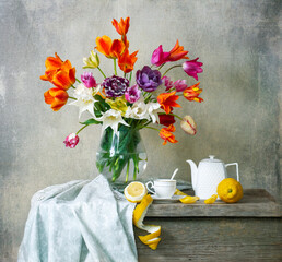 Still life with bouquet of tulips in glass vase, teapot, cup of tea and lemons on wooden table