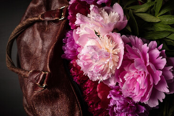 Bouquet of peonies lilac, burgundy and white, lie on an old leather travel bag, brown. Meeting or farewell.