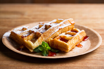 .Viennese waffles on a disposable plate with strawberry jam, icing sugar and mint. cook decorates dessert with icing sugar