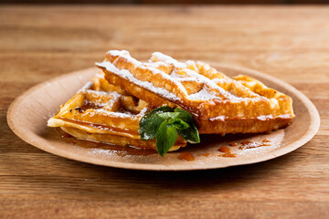 .Viennese waffles on a disposable plate with strawberry jam, icing sugar and mint. cook decorates dessert with icing sugar