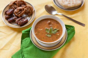 Moroccan food essentials for a Ramadan month table: Harira delicious and high nutritious food starter with dates and chebakia on the background with yellow negative space.