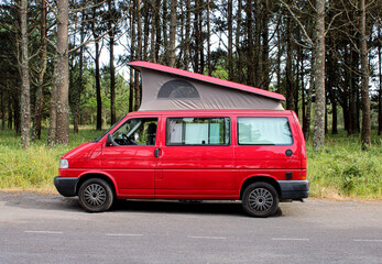 Red Van with roof up. Campervan parked next to forest.