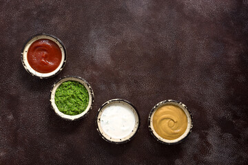 Assorted different sauce in the bowl: tomato, pesto, creamy with greens and mustard on a dark rustic background. Top view, copy space.