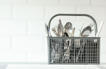 Gray plastic cutlery basket for dishwasher with fork, spoons and knifes on white background