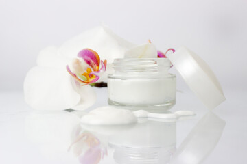 Cosmetic cream container and orchidea flowers and monstera leaf on white background