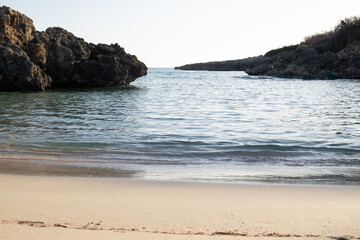 A view of a cove among the rocks of the Jonio sea water gently caresses the perfectly smooth sand, we are in southern Italy in Taranto.