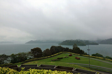 Fog over Cheo Lan Lake. Cloudy day, islets on the lake hide in the fog. In the foreground is a green lawn. Thailand.