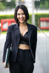 Asian young businesswoman walking and holding laptop on  blur urban background. 