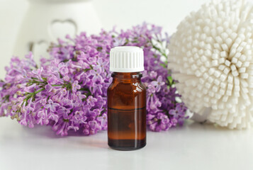 Small bottle with essential oil (tincture, infusion, perfume) and lilac flowers. Aromatherapy, spa and herbal medicine ingredients.