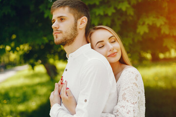Fototapeta premium A beautiful and gentle girl with light hair and a white dress is walking in a sunny summer forest with her handsome guy in a white shirt and dark pants...