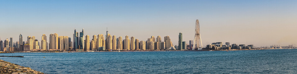 Fototapeta na wymiar Wide panoramic view of the Arabian Gulf and Dubai's skyline, visible from The Palm Jumeirah Boardwalk before the sunset. Dubai, United Arab Emirates