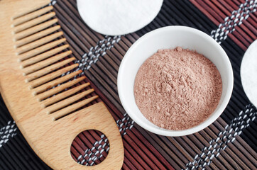 Pink bentonite clay powder in the small white bowl and hair brush. Clay texture close up. Diy facial or hair mask, dry shampoo recipe. Natural beauty treatment and spa. Top view, copy space
