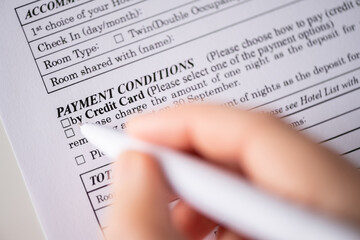 Woman customer filling hotel reservation form on the table at the office, payment conditionsby...