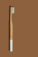 Bamboo toothbrush with a white handle and hard shadow on brown background. Zero waste, eco lifestyle. Biodegradable material. Vertical frame.