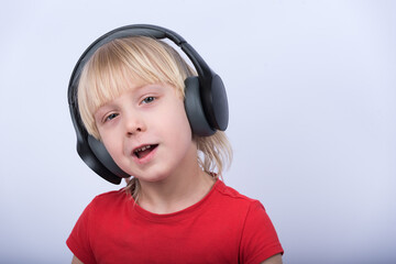 Portrait of blond boy with headphones on white background. Child listens to music.