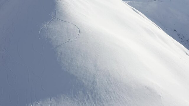 Aerial footage of a snowboarder riding down a mountain.