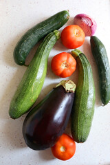 Homegrown summer vegetables on the kitchen counter: tomato, zucchini, cucumber, eggplant and purple onion. Top view.