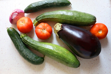 Homegrown summer vegetables on the kitchen counter: tomato, zucchini, cucumber, eggplant and purple onion. Top view.
