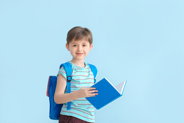 Cute little schoolboy with book on color background