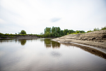 Layers of sand on the beach formed by waves and tides, layers of white sand on the shore along the river Tara. Beauty of the Siberian expanses. Forest along the coast.