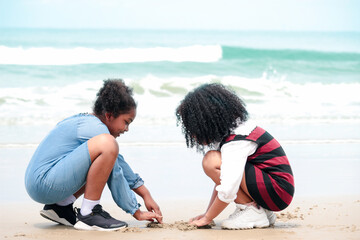 Fototapeta na wymiar Cute kids having fun together on sandy summer with blue sea, happy girls friend making sand castle, playing with sandat on tropical beach