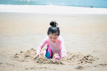 Cute kid having fun on sandy summer with blue sea, happy little girl making sand castle, playing with sandat on tropical beach