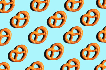 Pattern of salted pretzels with a hard shadow on a light blue background.