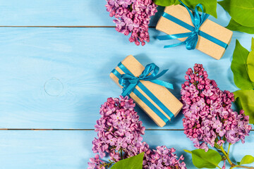 Two gift boxes with lilac flowers on a light blue wooden background with the possibility of copying the space.