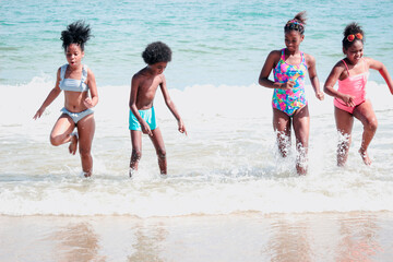 Groupmboys and girls running and makeing splashes in shallow sae water, cute kids having fun on sandy summer beach, happy childhood friend playing together on tropical beach