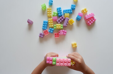 Close up of child's hands playing with colorful plastic bricks at the table. Toddler having fun and building out of bright constructor bricks. Early learning. stripe background. Developing toys