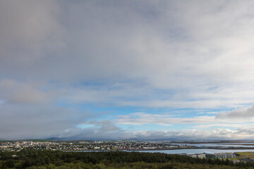 A cityscape of Reykjavík, the capital and largest city of Iceland, photographed from a hill on a cloudy summer day.