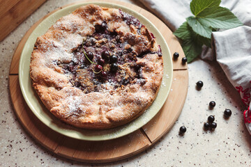 Realistic homemade blackcurrant pie on the kitchen table next to a linen apron and green leaves with berries. Top view.