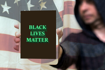 Selective focus Portrait of a hooded white man holds tablet with the inscription Black Lives Matter. protests of racial discrimination.Usa flag blurred background