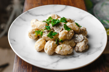 Potato gnocchi, Italian potato dumplings with cheese sauce, mushrooms and herbs on a plate. Side view, top view