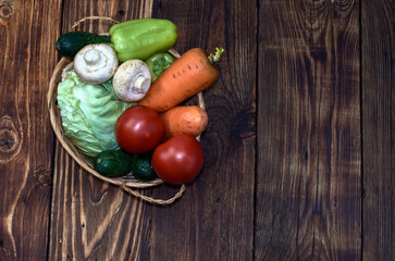 vegetables are collected in a small basket on a wooden table, top view, carrots, sweet green peppers, tomatoes, cucumbers, mushrooms, champignons, half a cabbage cabbage, healthy food, diet food