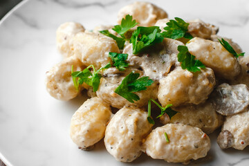 Potato gnocchi, Italian potato dumplings with cheese sauce, mushrooms and herbs on a plate. Side view, top view