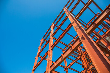 Red steel beam construction site against a bright blue sky