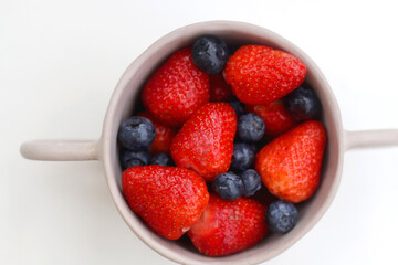 Ceramic bowl with fresh blueberries and strawberries. Top view, white background.