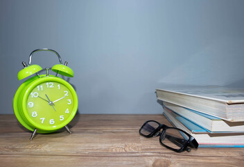 Green clock,spectacle and a bunch of books in grey background.Time and health concept 