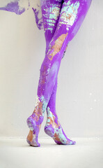 Fototapeta premium View from behind on beautiful legs and feet of a sexy young artistically abstract painted woman with white, blue and purple and paint. Creative body art painting, copy space.