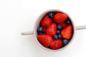 Ceramic bowl with fresh blueberries and strawberries. Top view, white background.