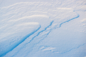 Beautiful winter background with snowy ground. Natural snow texture. Wind sculpted patterns on snow surface.