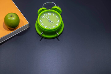 Green alarm clock with green apple on top of an orange books in black background.Flat lay. Healthy concept